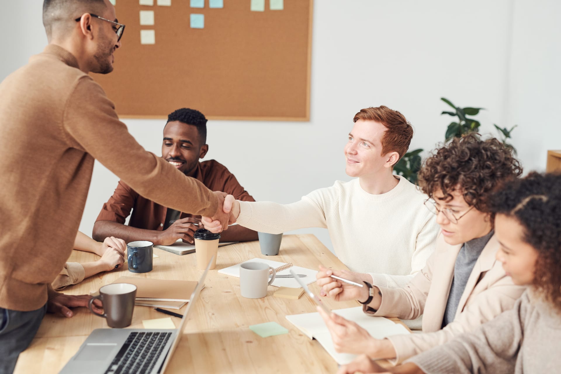 Eine Führungsperson schüttelt die Hand eines Mitarbeiters während eines Team-Meetings. Sinnbild für gruppenorientierte Führungsstile.