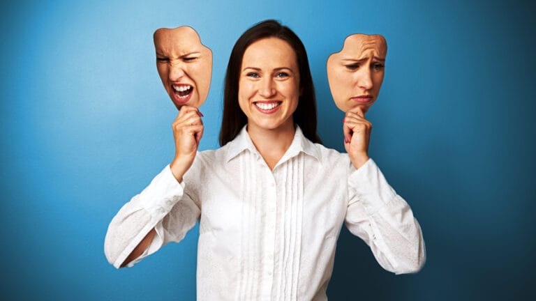 Eine Geschäftsfrau hält zwei Masken, die unterschiedliche Emotionen darstellen: eine wütende und eine traurige, während sie in der Mitte lächelt. Sie steht vor einem blauen Hintergrund – eine perfekte Metapher für Transaktionsanalyse nach Eric Berne im Coaching und Management.