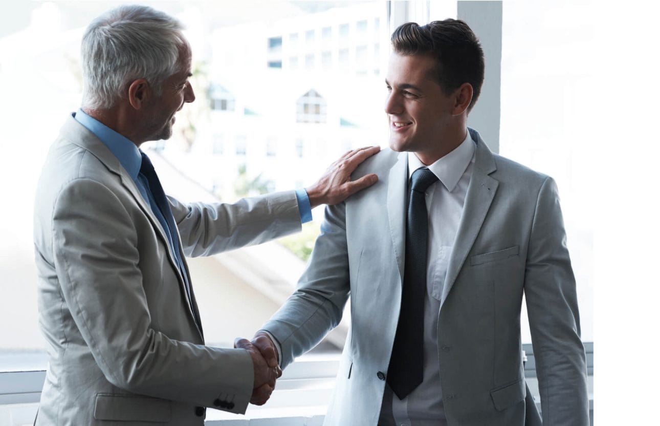 Ein Geschäftsmann schüttelt seinem Geschäftspartner die Hand und legt als Zeichen der Wertschätzung eine Hand seine Schulter