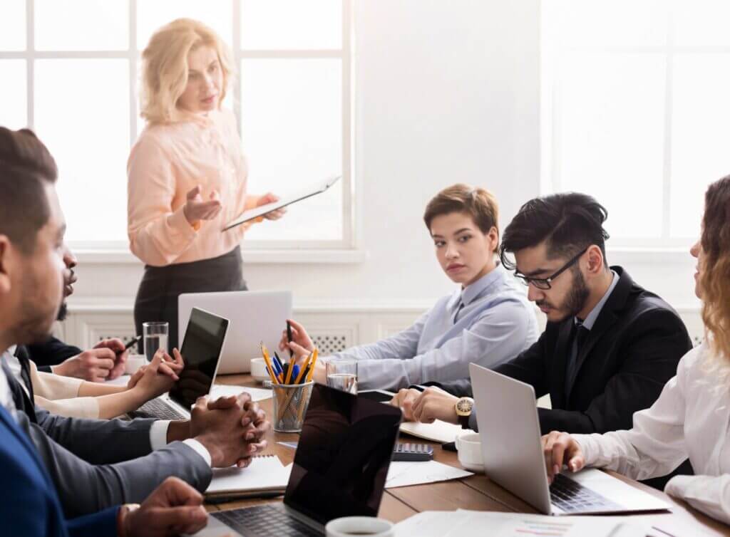 Ein Mitarbeiter schaut mit beschämtem Blick nach unten, während eines Meetings. Seine Teamleiterin und Kollegen blicken auf ihn.