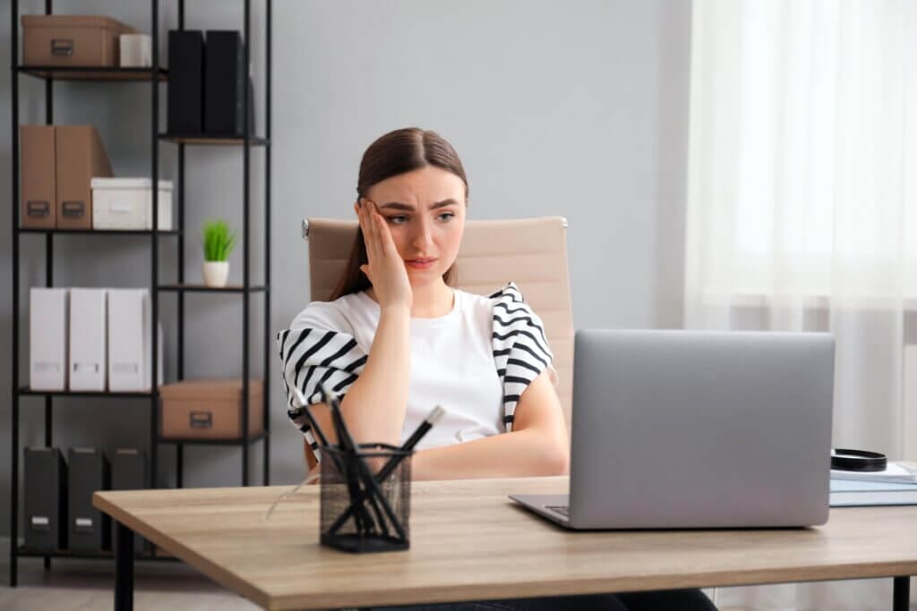 Eine junge Mitarbeiterin schaut beschämt auf den Bildschirm ihres Notebooks, als sie eine unangenehme Nachricht darin sieht.