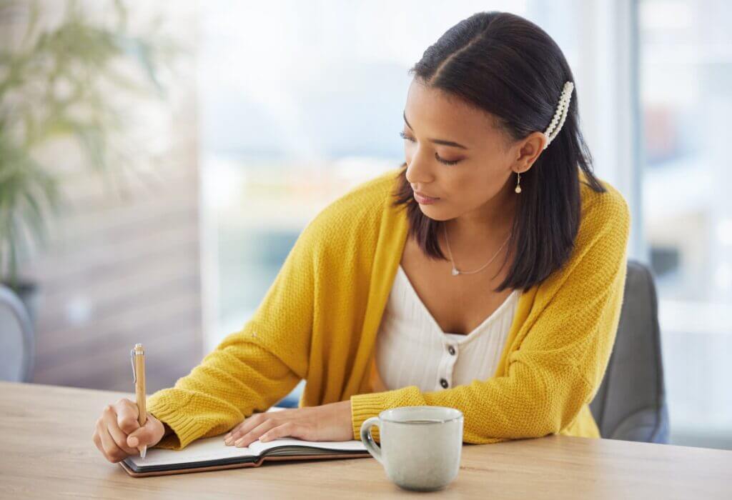 Mit dem Journaling hält eine junge Frau ihre Gedanken in einem Notizbuch während der Selbstreflexion fest.