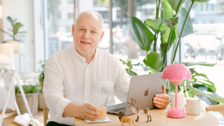 Life & Business Coach Mathias Hühnerbein aus Fürth sitzt lächelnd am Tisch vor einem Notebook.