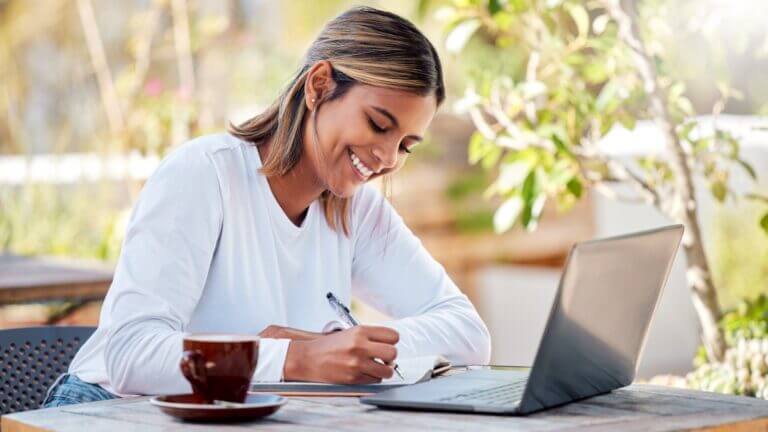 Eine Frau folgt auf dem Laptop einer Online-Fortbildung und schreibt Notizen ins Heft. Symbolisches Bild für den proCEO Online CAMPUS.