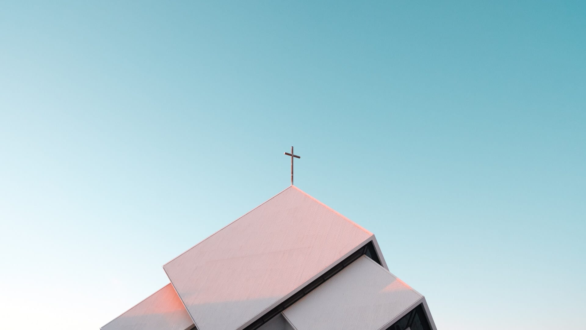 Das Kreuz auf der Dachspitze einer Kirche ragt in den blauen Himmel. Symbolisch für karitative Dienste und diakonisch-kirchliche Einrichtungen.
