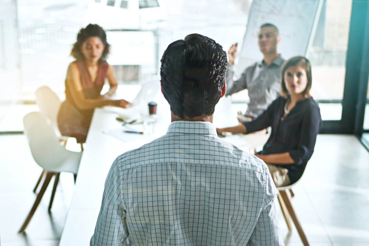 Ein Supervisor steht im Meetingraum vor einer Gruppe von Mitarbeitern während eines Teamcoaching.