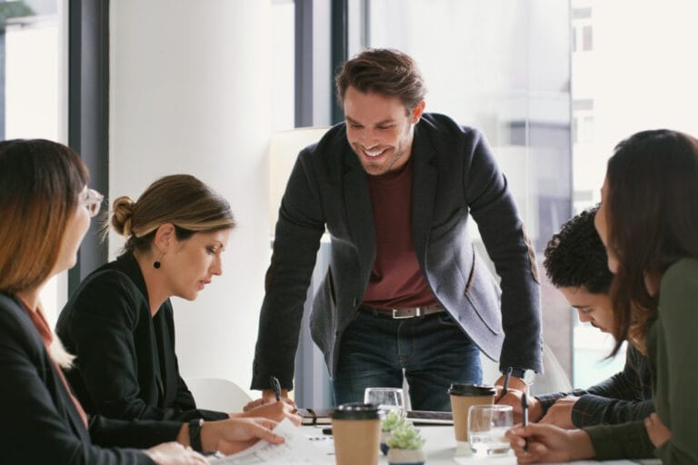 Ein selbstständiger Berater spricht zu einem Team in einem Meetingraum. Sinnbild für eine freiberufliche Karriere nach einer Supervision Ausbildung.